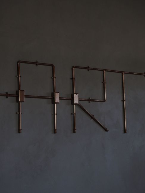 Minimalist metal pipe art spelling 'ART' on a dark wall creates a modern aesthetic.